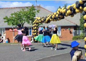 Image of 'Dreamgirls' performance. Performers are wearing polka-dotted skirts and there is a black and gold balloon arch in the background