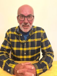 Paul O'Byrne smiling, wearing a black and yellow checked shirt