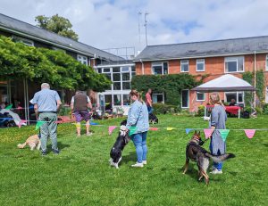 Image of The Scruffies 2024- people are on a lawn with their dogs surrounded by colourful bunting