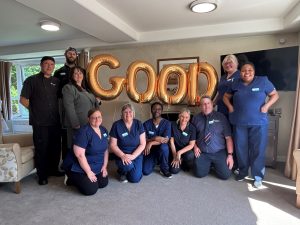 Sanctuary Care staff smiling with gold balloons that spell 'good' after their 'Good' rating from the CQC